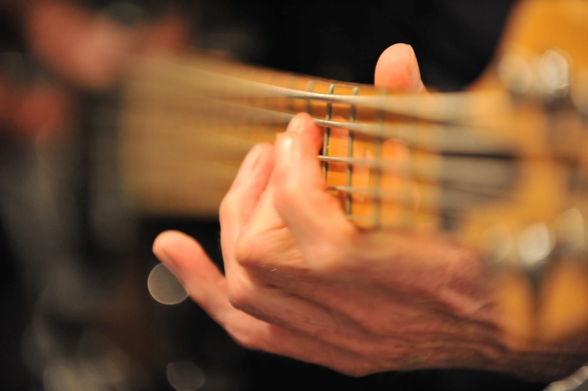 A musician's hand holds a note on the neck of a bass guitar in warm, soft-focus light