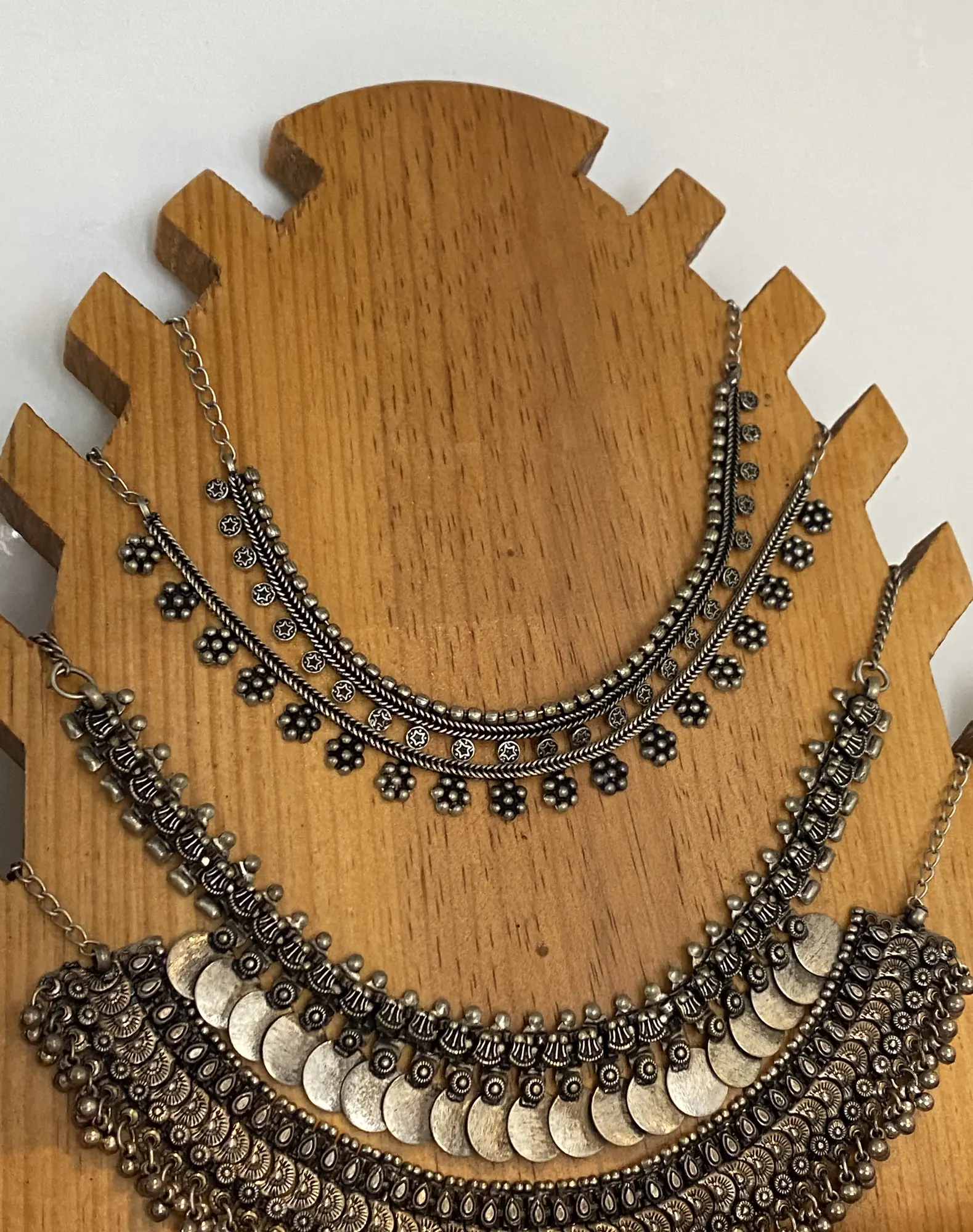 Three oxidised silver statement necklaces with coin and filigree details hang on a wooden display bust