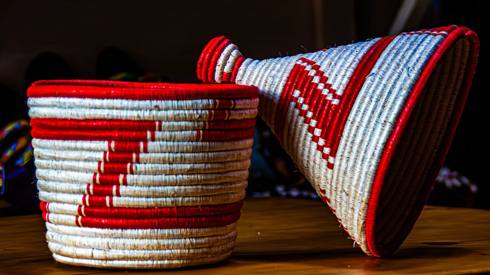 Two coiled woven baskets in white with red zigzag stripes sit on a wooden surface, one tipped on its side